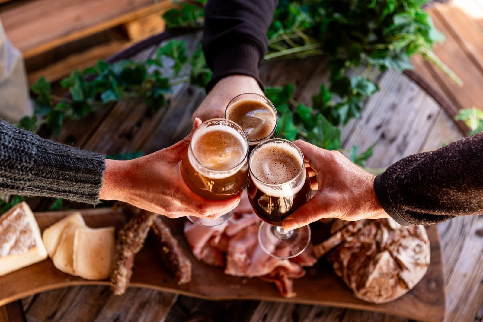 Trois verres de bière de La Bièrataise qui trinquent au-dessus d'une planche de charcuterie et de fromage
